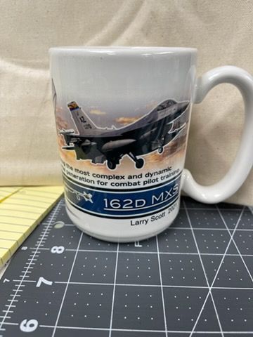A white mug featuring a graphic of an F-16 fighter jet, the text